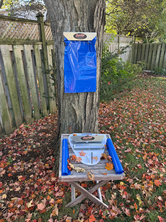 The First Tap™ kit in use: Sapsuckers® sap bag holder and sap bag hung on a backyard maple, with the kit parts on a table