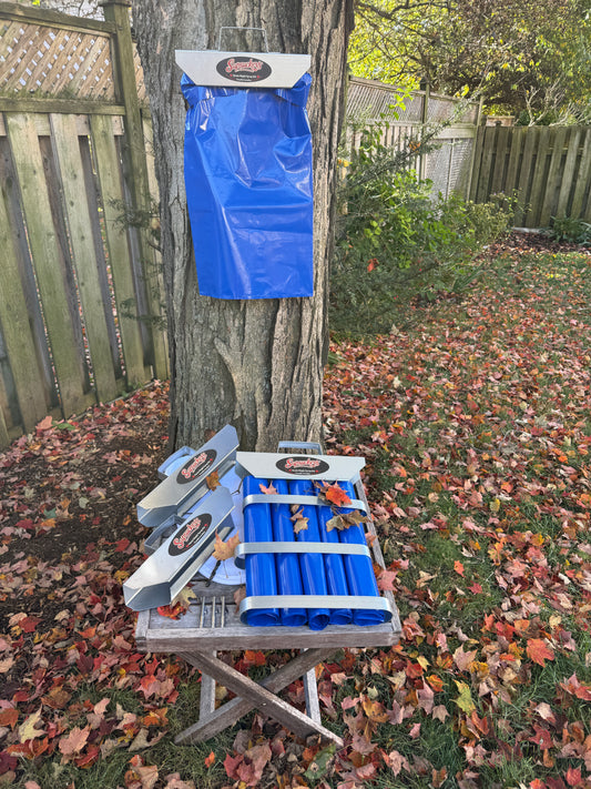 The Triple Tap™ kit in use: sap bag holder and sap bag hung on a backyard maple, with three holders, sap bags, spiles and filter on a table